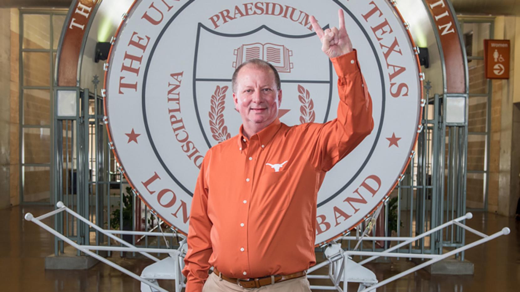 Tx engineering alumnus Rick Church standing in front of UT Austin band logo