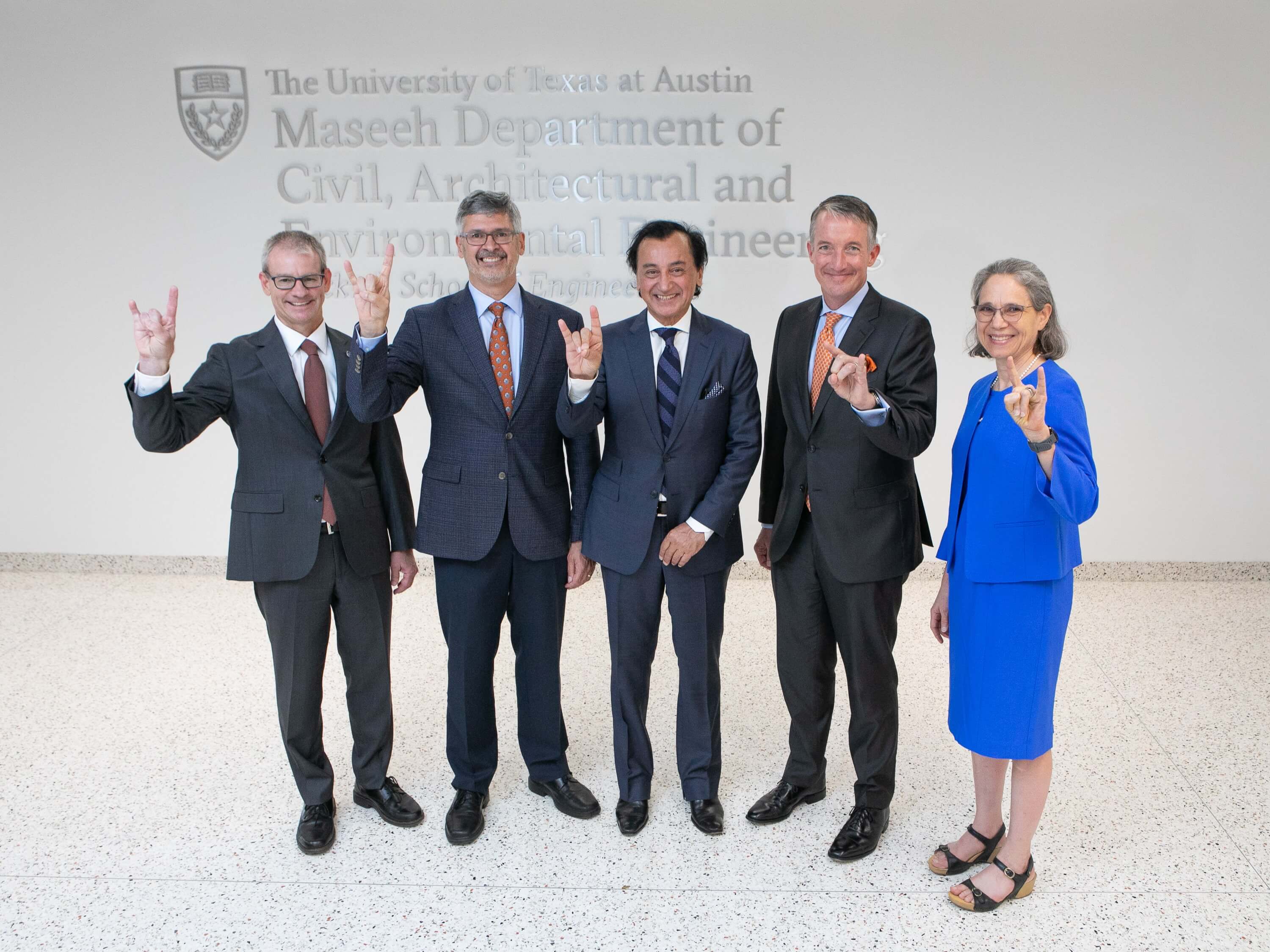 Fariborz Maseeh and UT Austin leadership doing hook 'em horns hand sign in front Maseeh building engraving