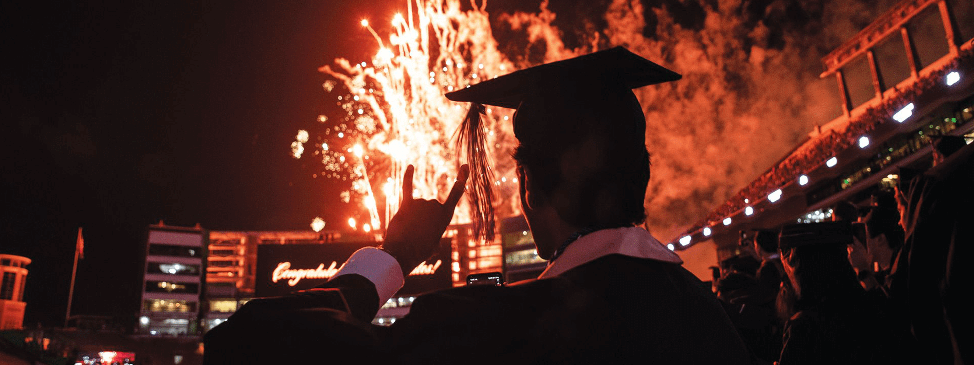 Texas engineering student in graduation cap lit up by fireworks