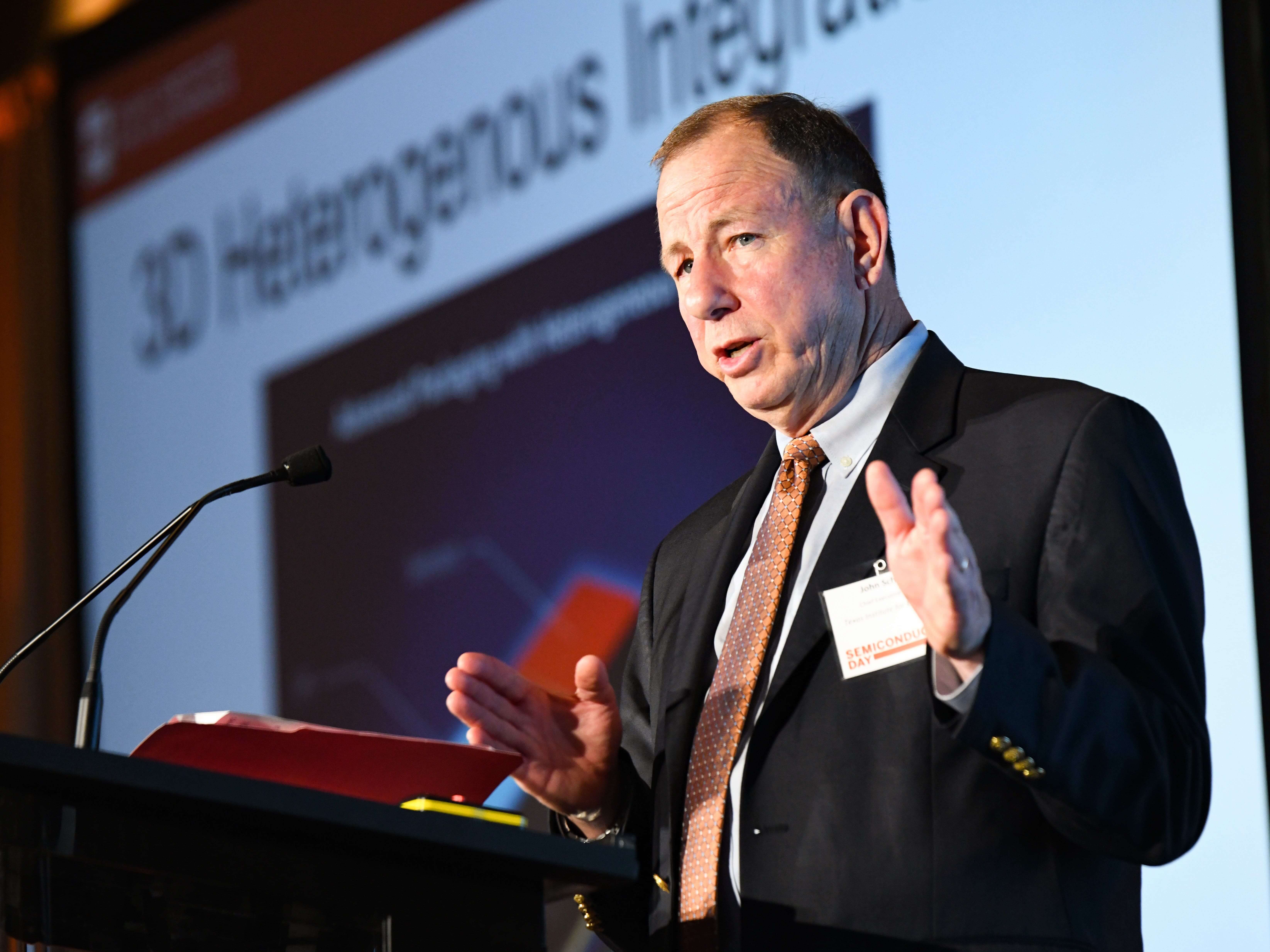 John Schreck speaking on stage at a podium