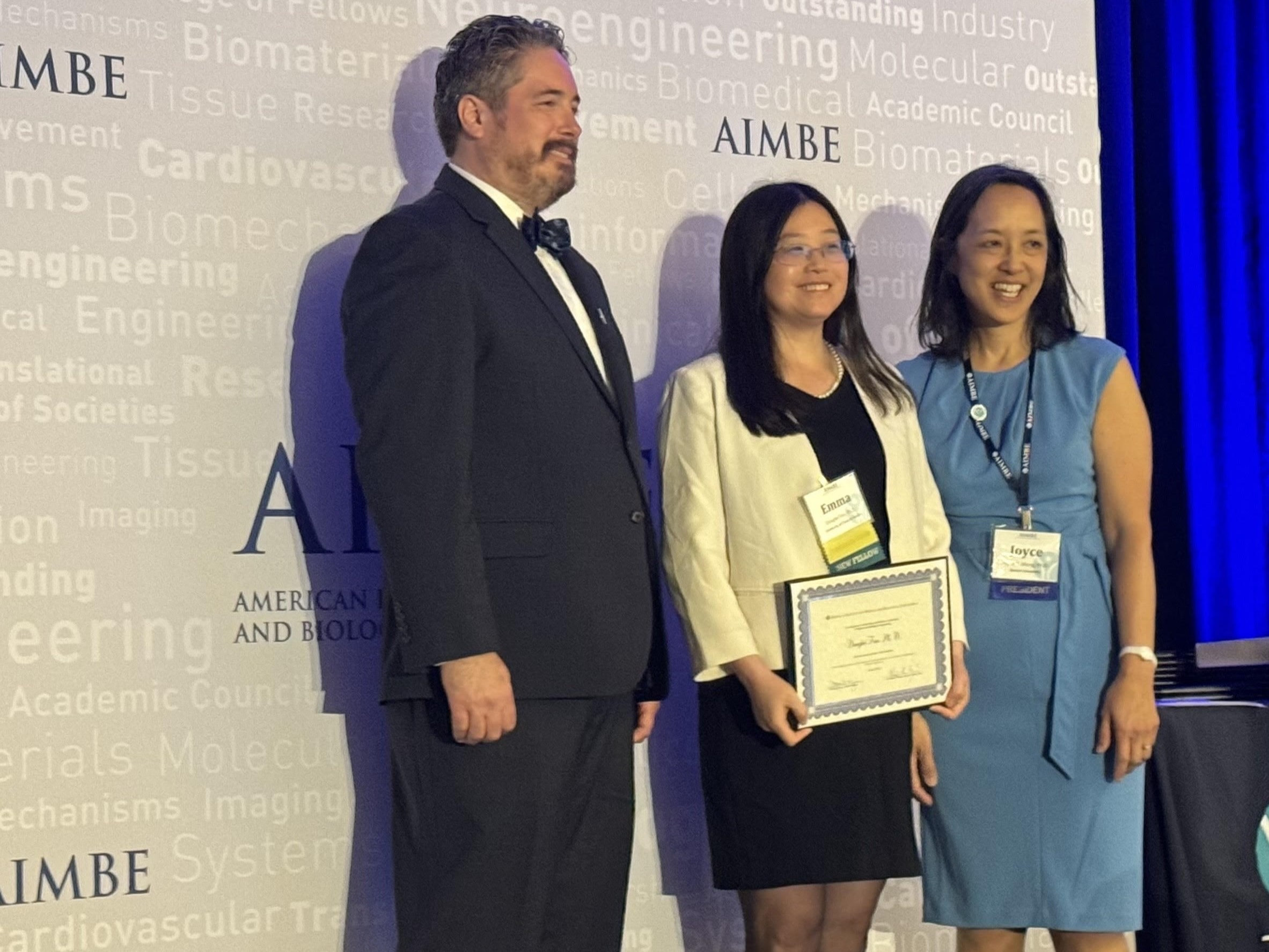 Emma Fan smiling for photos while holding AIMBE certificate