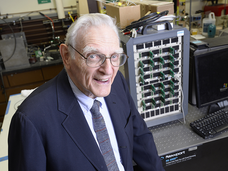 Portrait of John Goodenough in the lab standing in front of some of his equipment