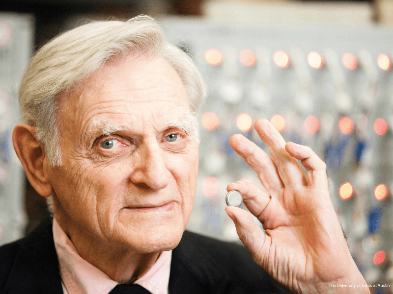 John Goodenough smiling while holding a lithium-ion battery