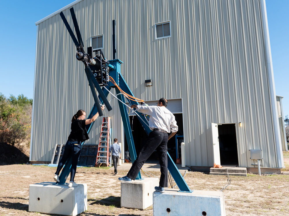 Chloe Johnson and Jayant Sirohi standing on cinder blocks working on a rotor