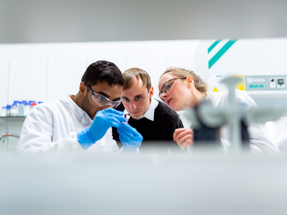 Texas engineers wearing gloves and looking at small device in a lab