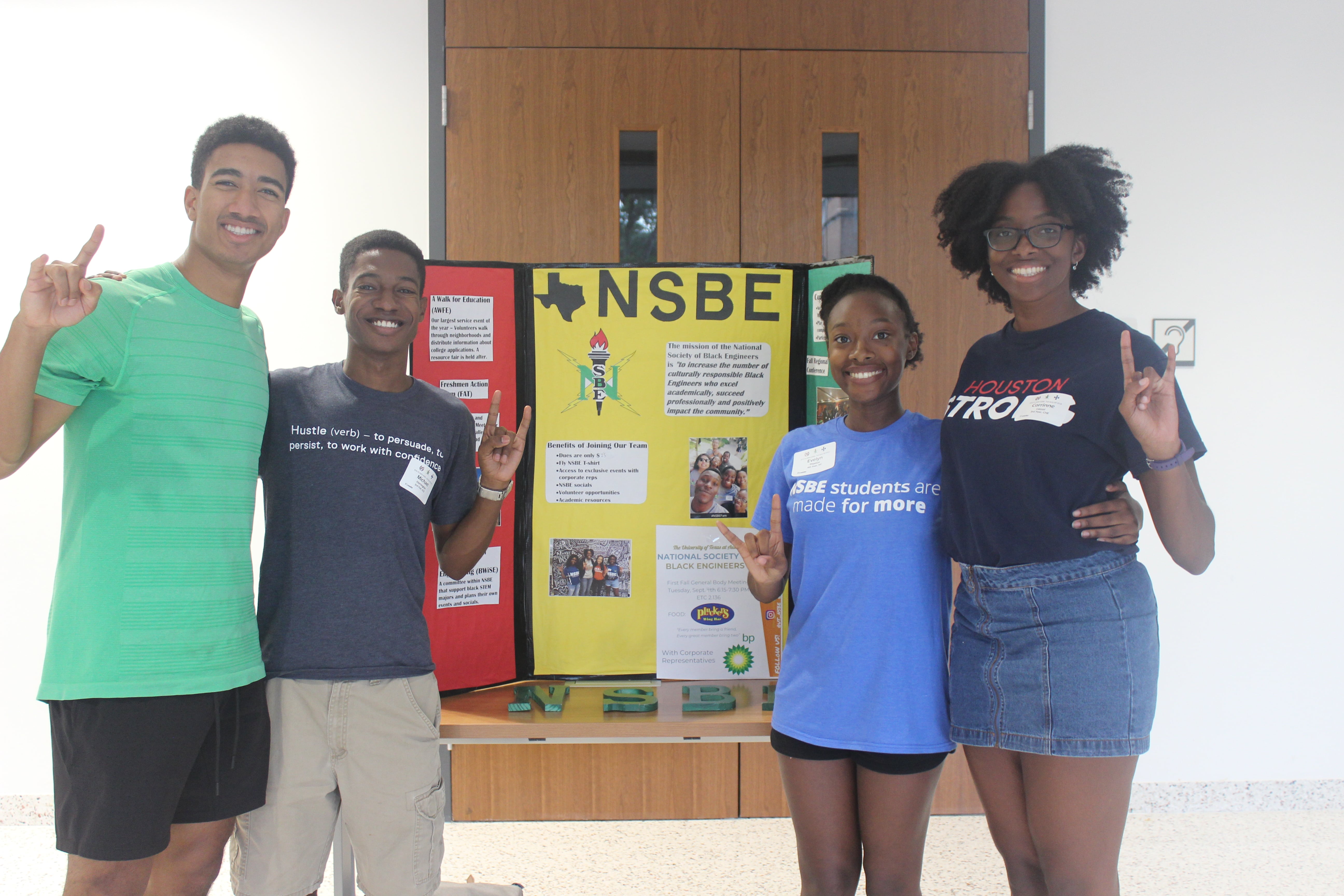 Texas engineering students smiling in front of a NSBE poster