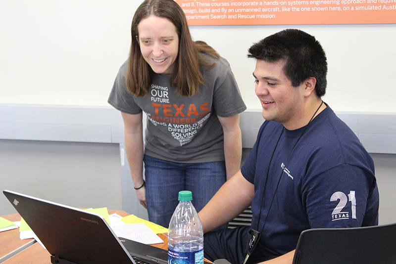 Texas engineers wearing UT Austin t-shirts smiling while looking at laptop