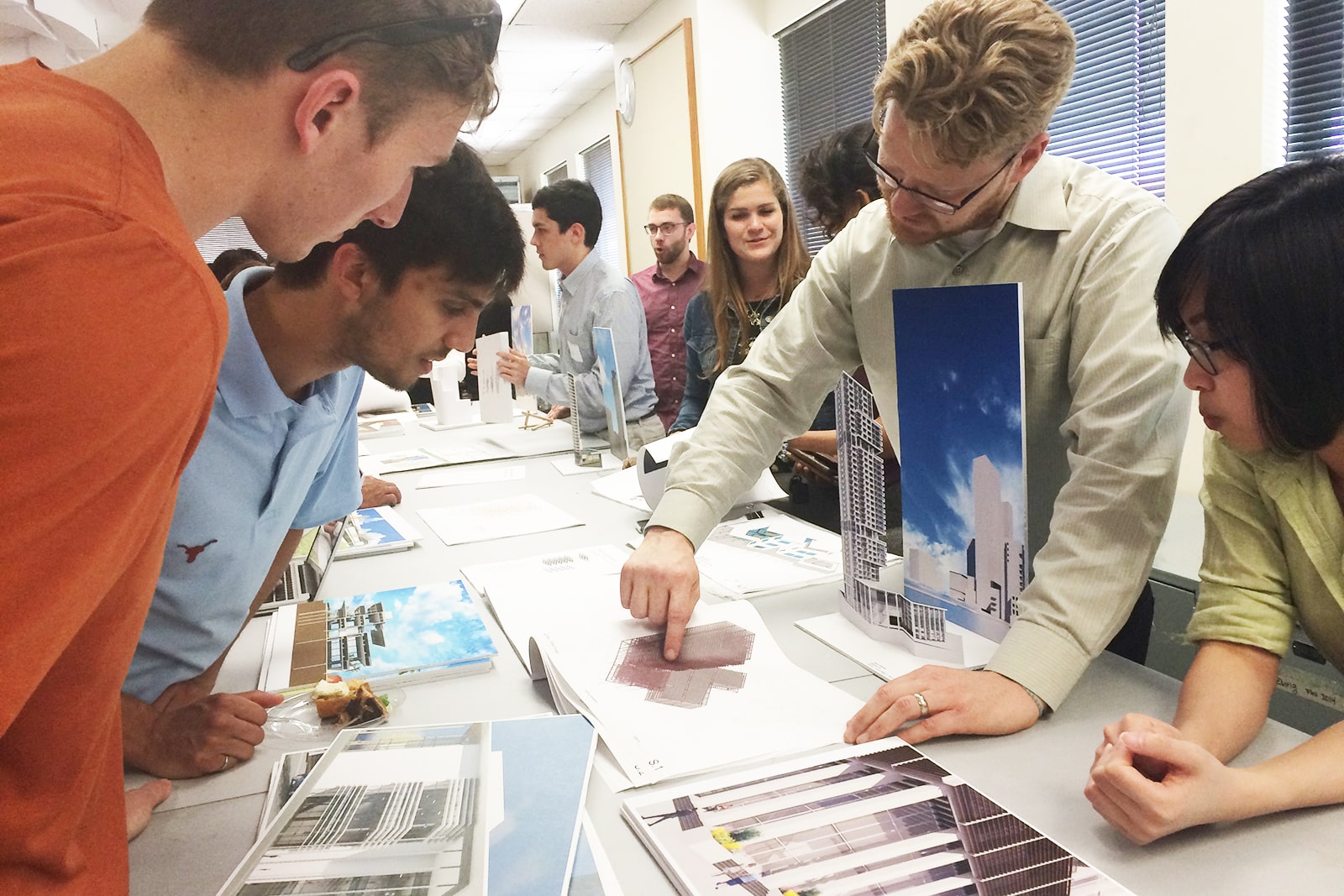 professor showing students architectural diagrams on large table