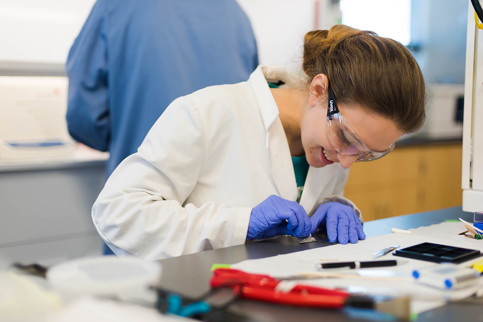 student in lab coat and goggles writing at a desk